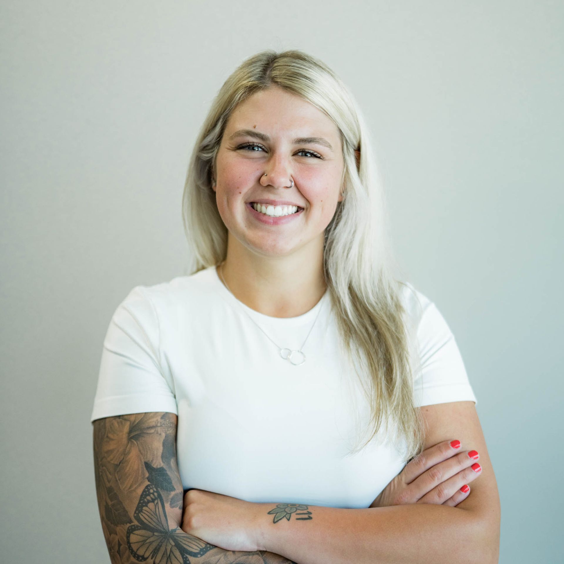 A woman with a tattoo on her arm is smiling with her arms crossed.