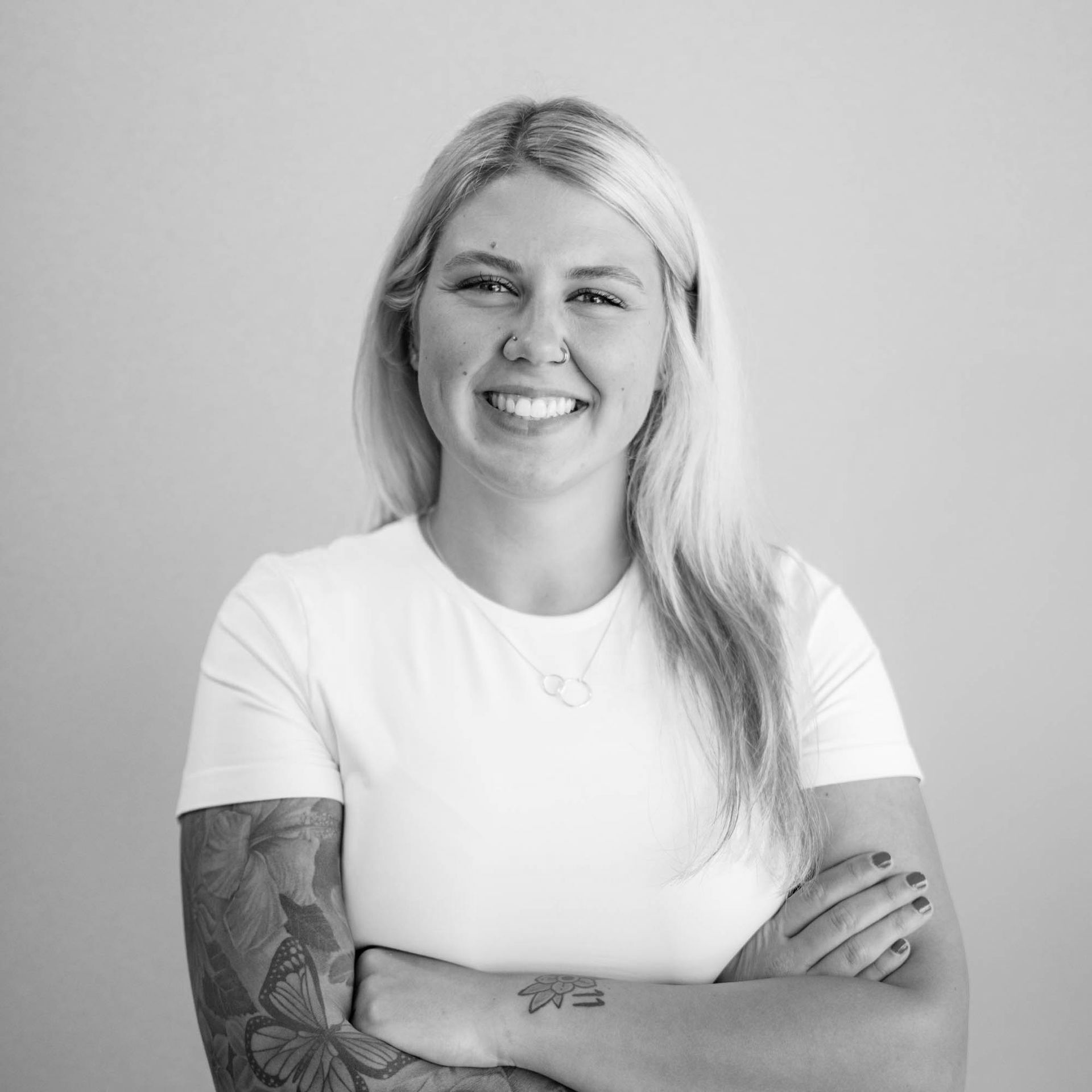 A woman with a tattoo on her arm is smiling in a black and white photo.