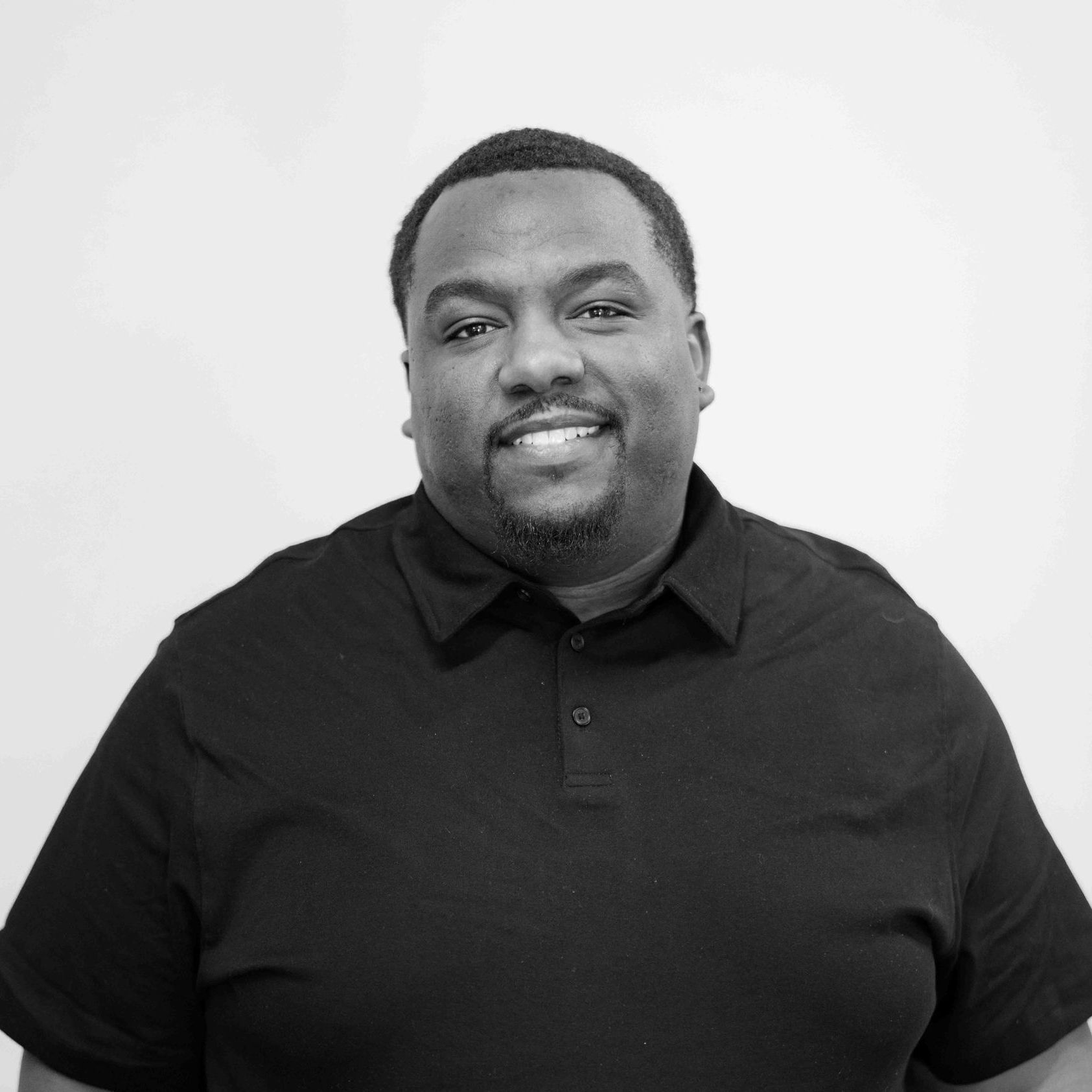 A black and white photo of a man wearing a black shirt and smiling.