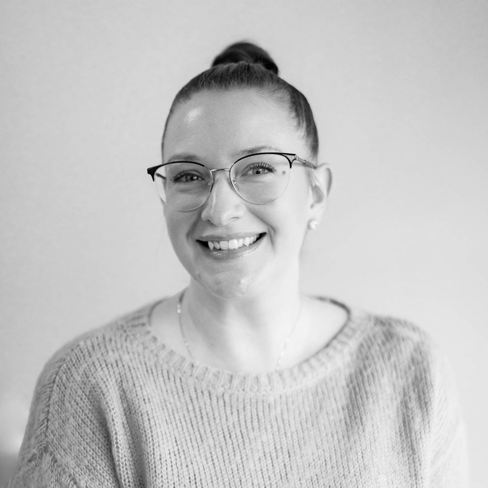 A woman wearing glasses and a sweater is smiling in a black and white photo.