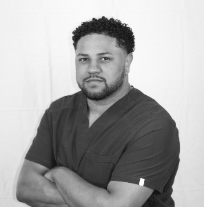 Person with crossed arms in dark scrubs, posing against a plain light background.