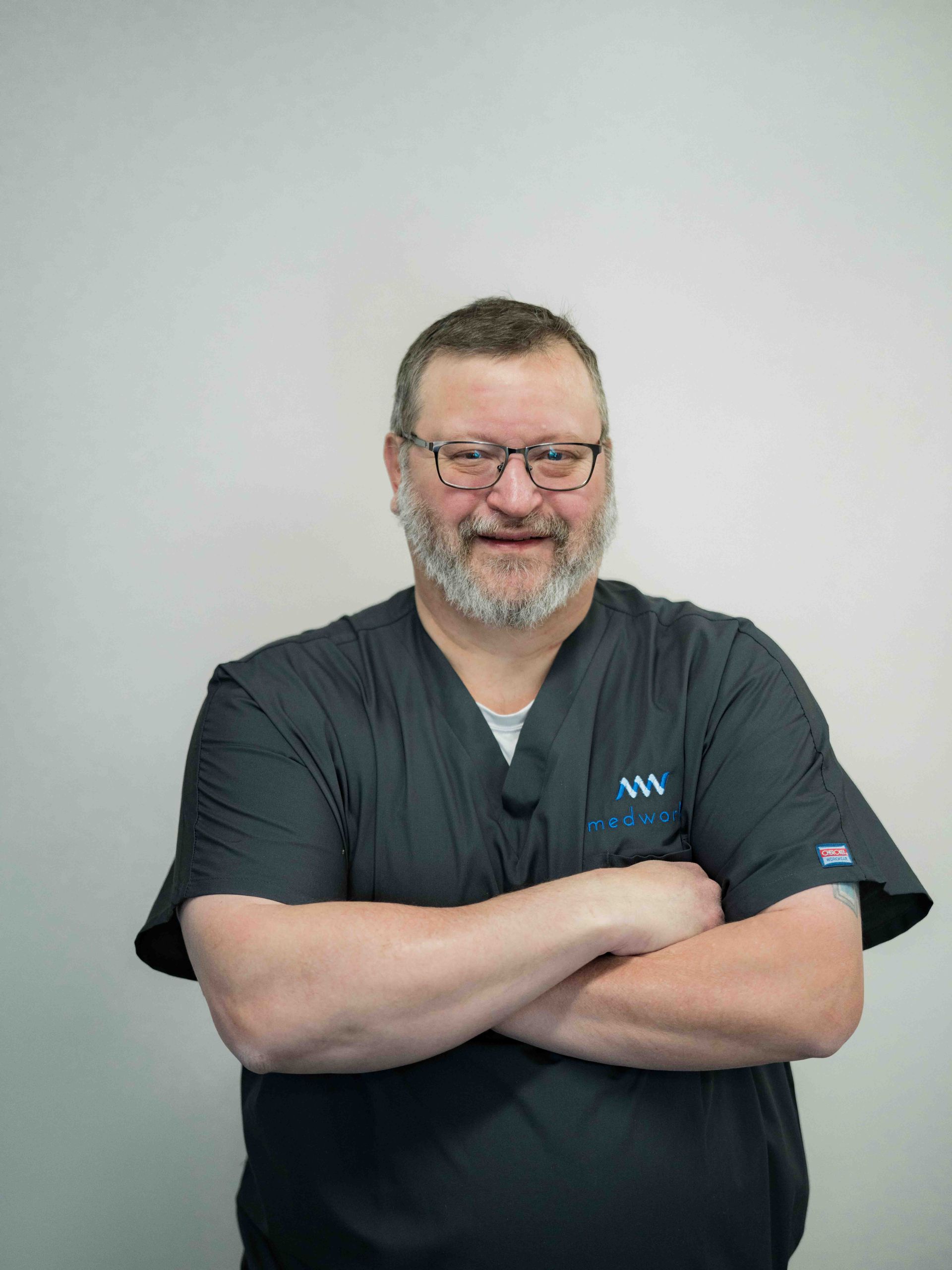 A man with a beard and glasses is standing with his arms crossed.