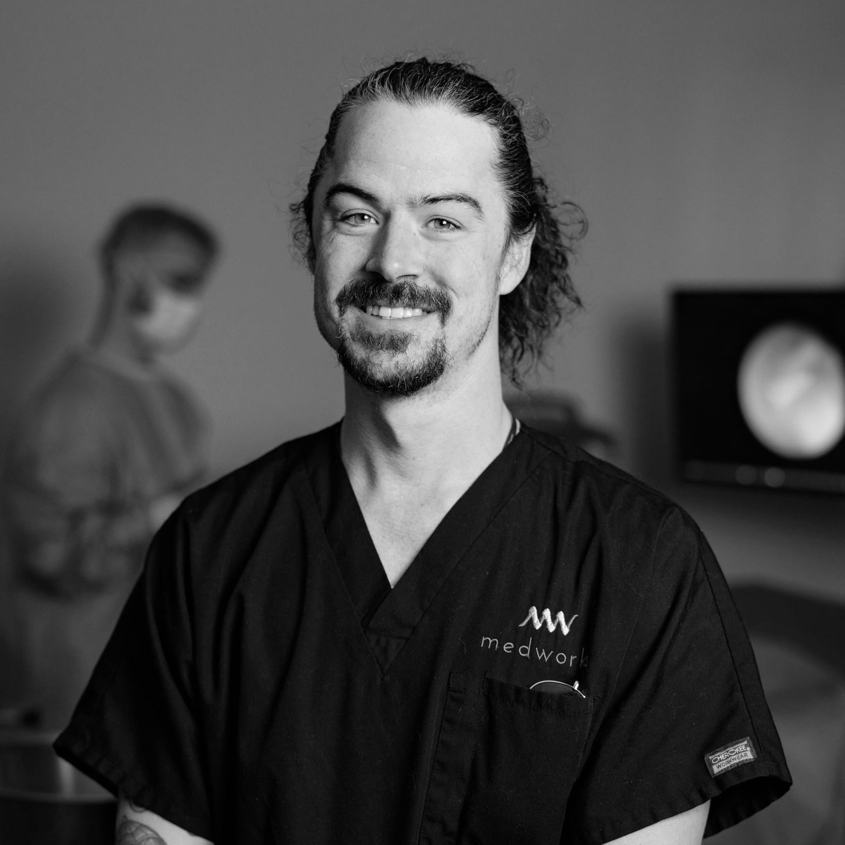 A black and white photo of a man wearing scrubs