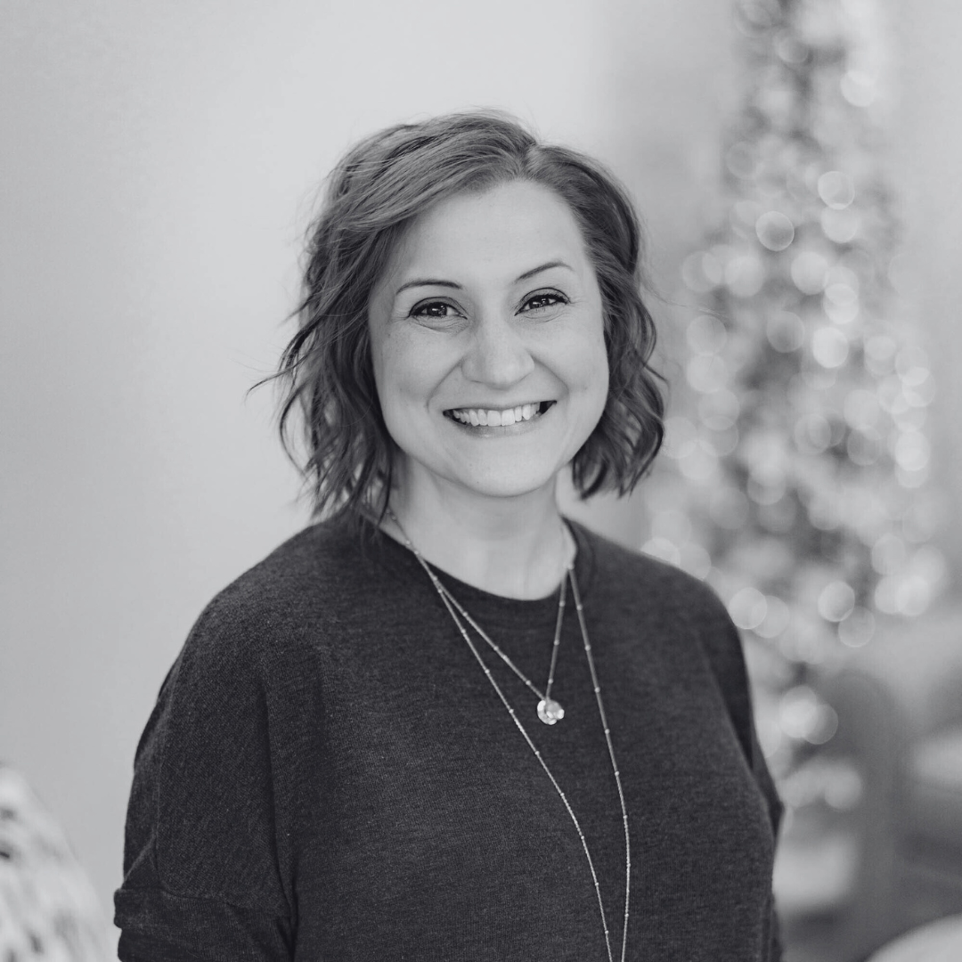 A woman wearing a black sweater and a necklace is smiling in a black and white photo.