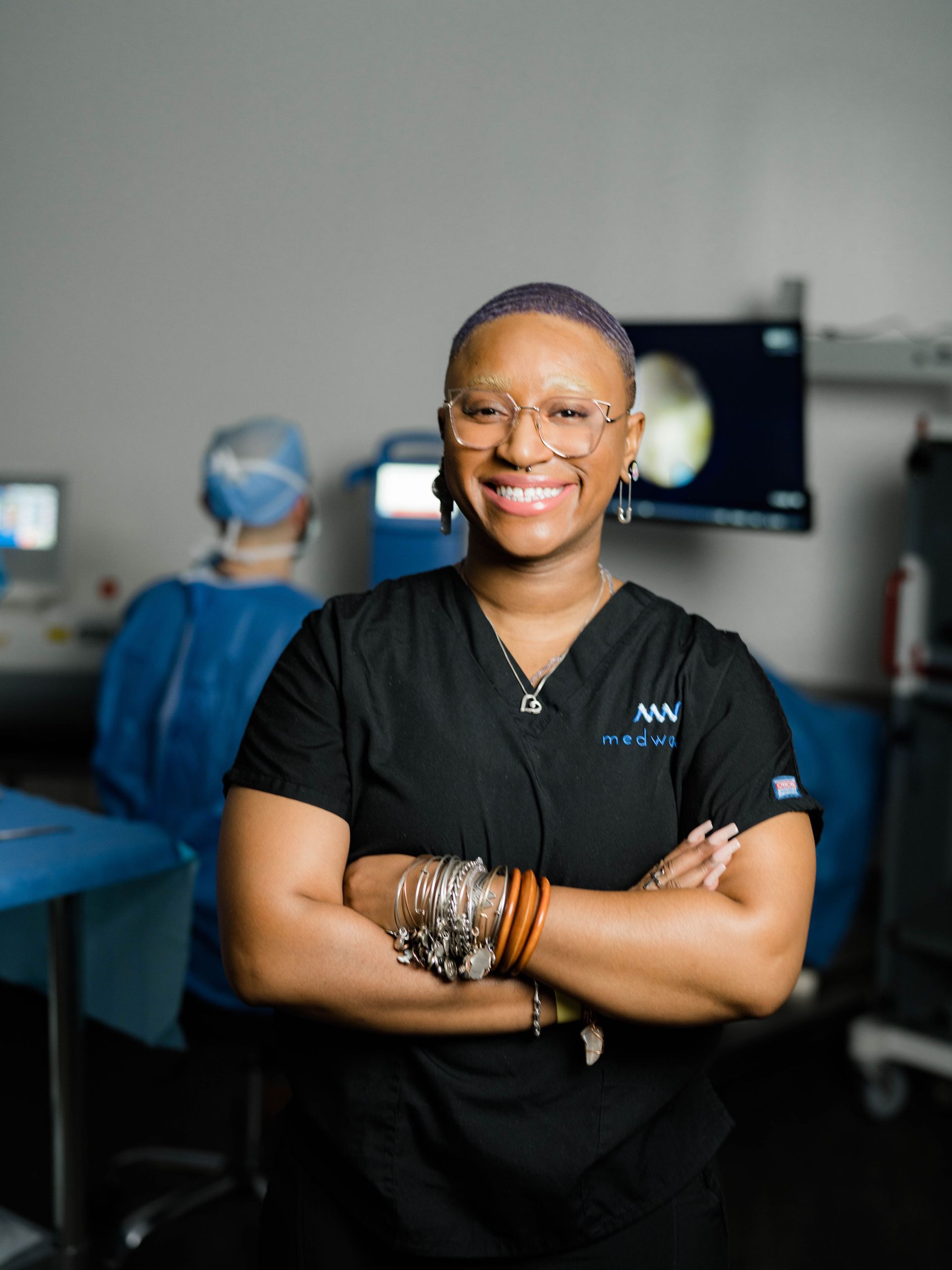 A woman in a black scrub top is posing for a picture with her arms crossed.
