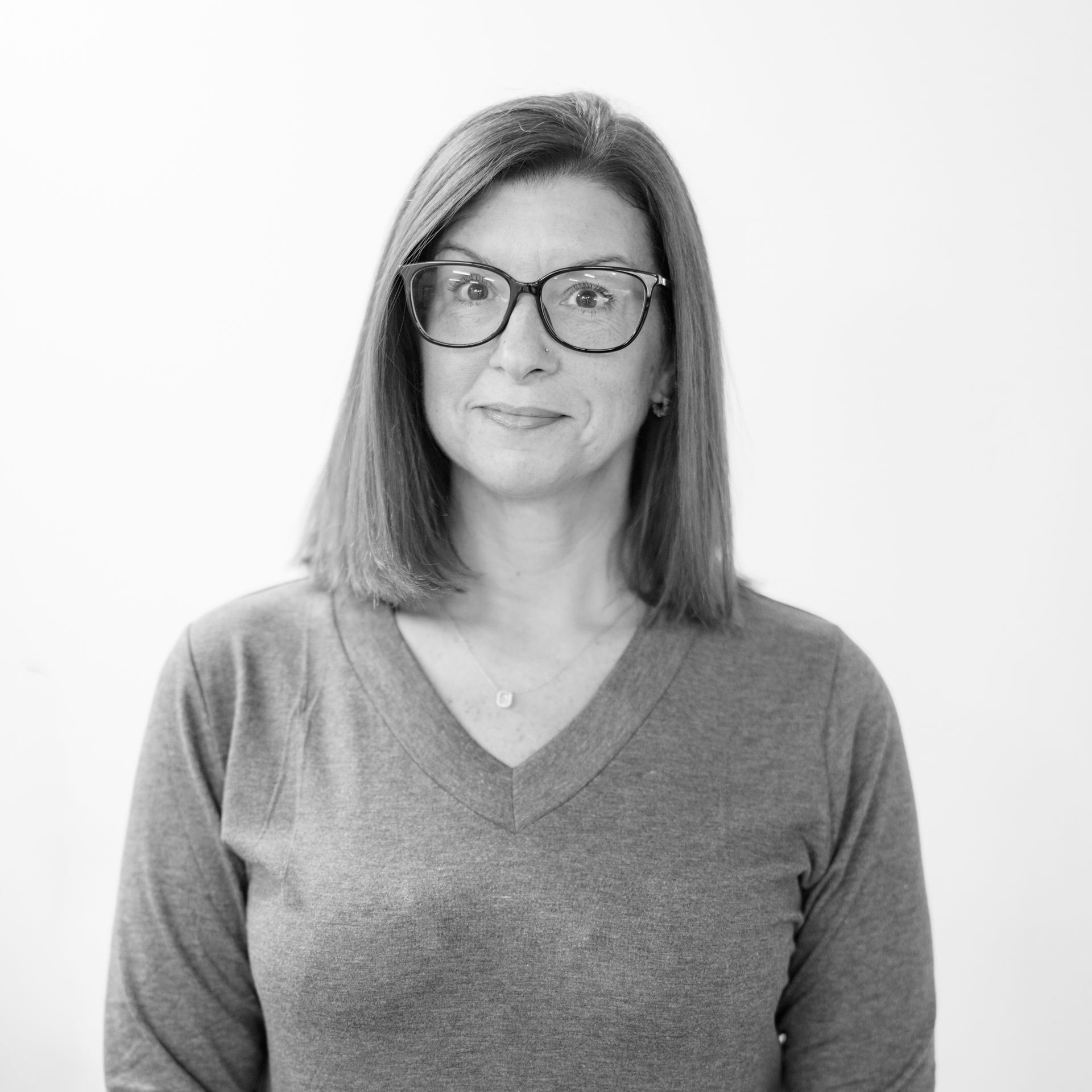 Black-and-white portrait of a woman wearing glasses and a V-neck sweater, facing forward and smiling softly