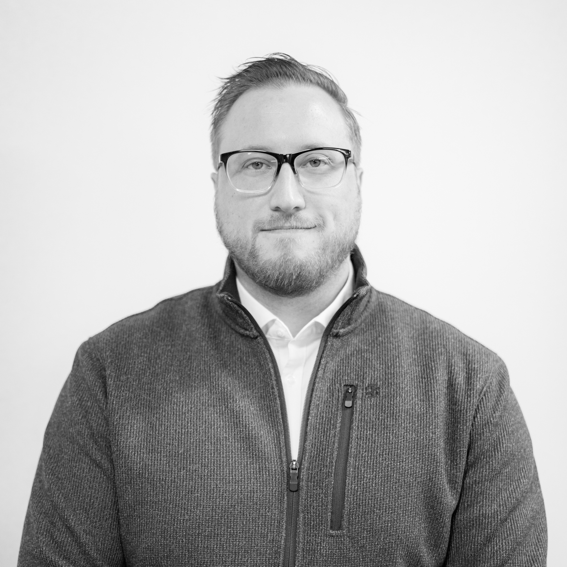 Portrait of a man wearing glasses and a dark zip-up sweater against a plain background