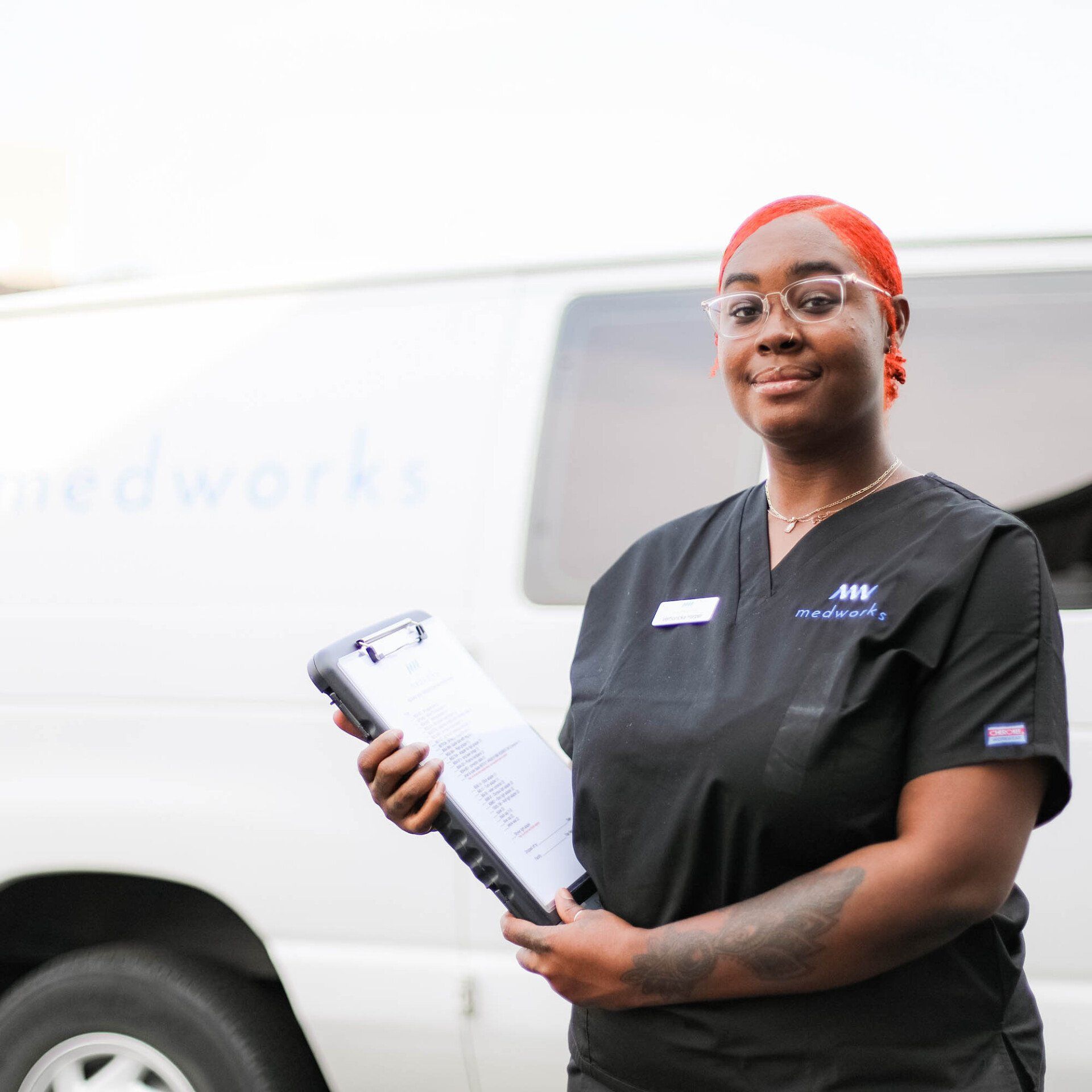 A woman holding a clipboard in front of a van that says medworks