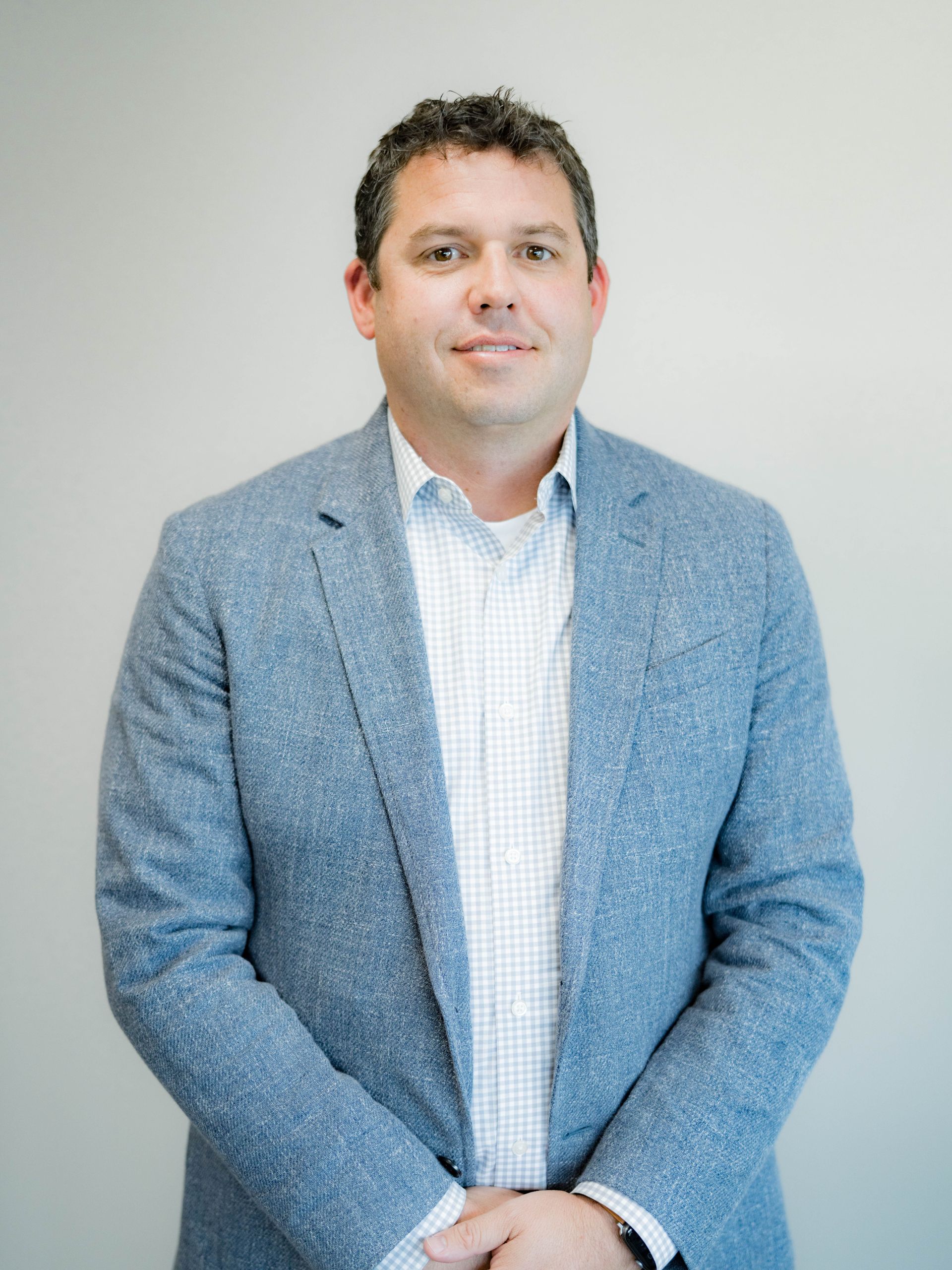 A man in a blue jacket and white shirt is standing in front of a white wall.