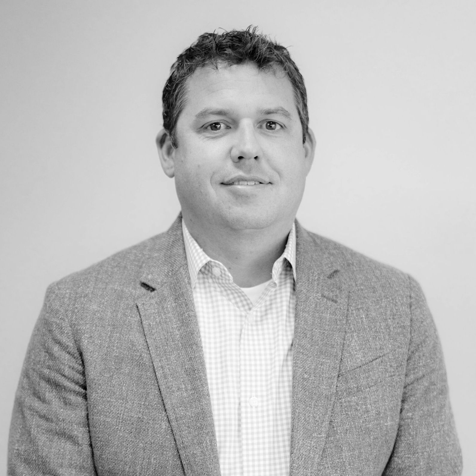 A man in a suit and white shirt is smiling in a black and white photo.