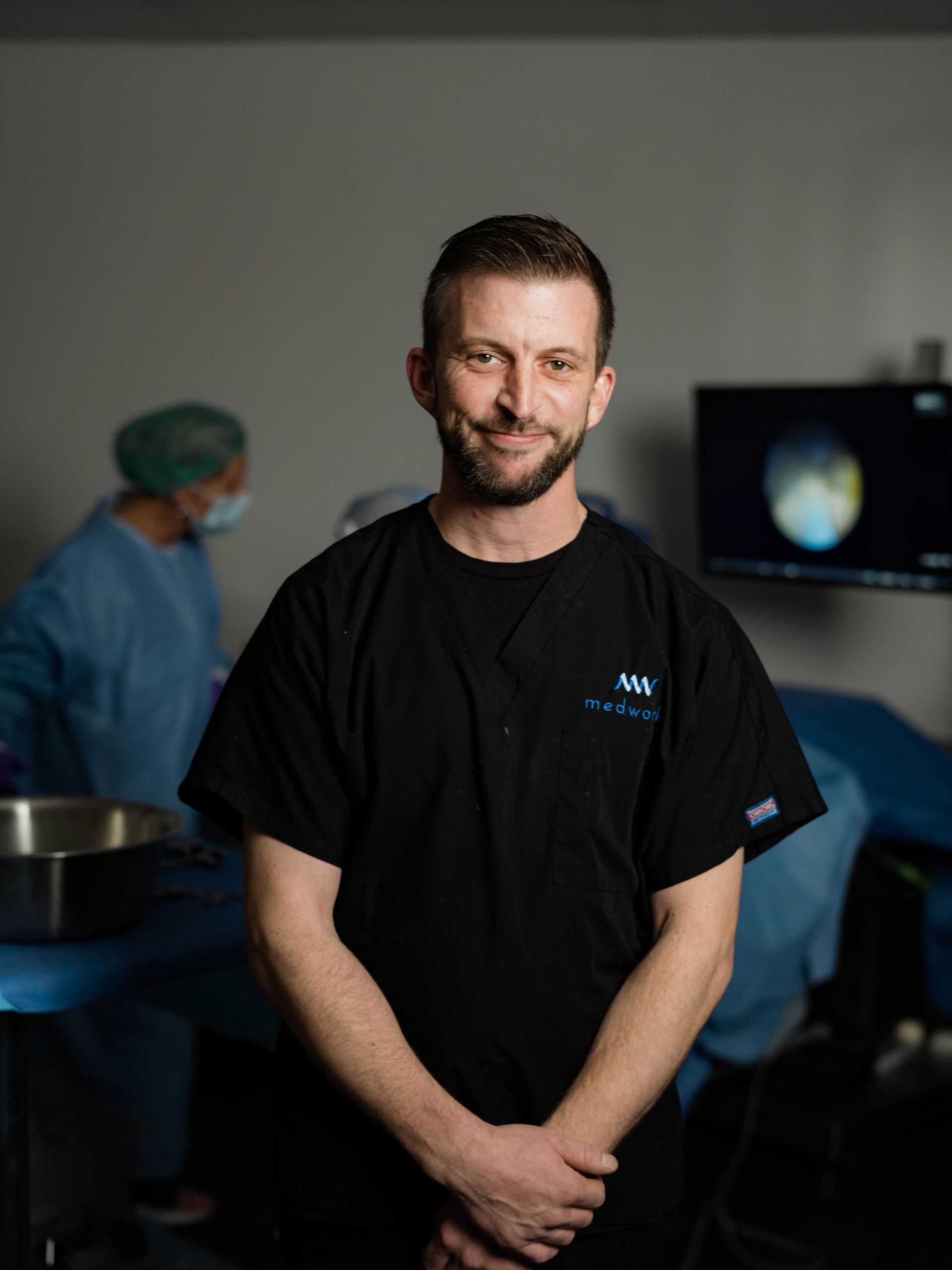 A man in a black shirt is standing in an operating room.