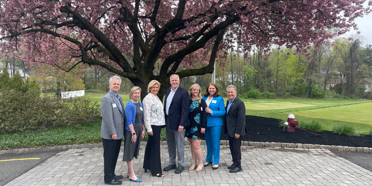 Family Investors team posing in a park under a blooming pink tree, with greenery and a path behind them.