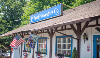 Family Investors office with blue sign, hanging flowers, and an American flag under a shingled roof
