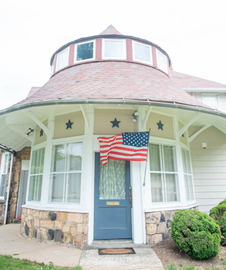 Round white house porch with blue door and windowed turret, decorated with an American flag and stars.