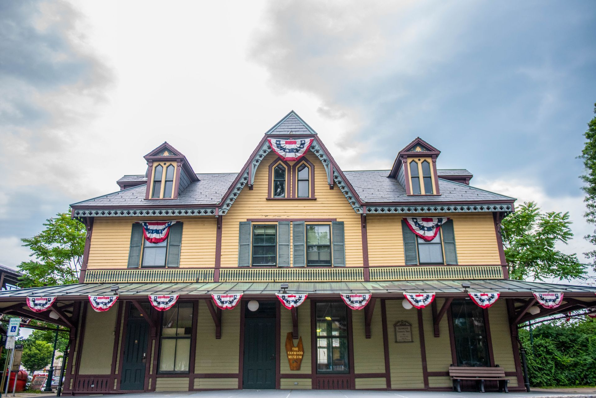 Historic yellow Victorian-style building with red, white, and blue bunting under a cloudy sky