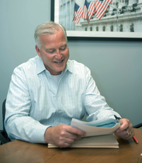Pete Chemidlin from Family Investors in a light blue shirt reading papers at a desk in an office