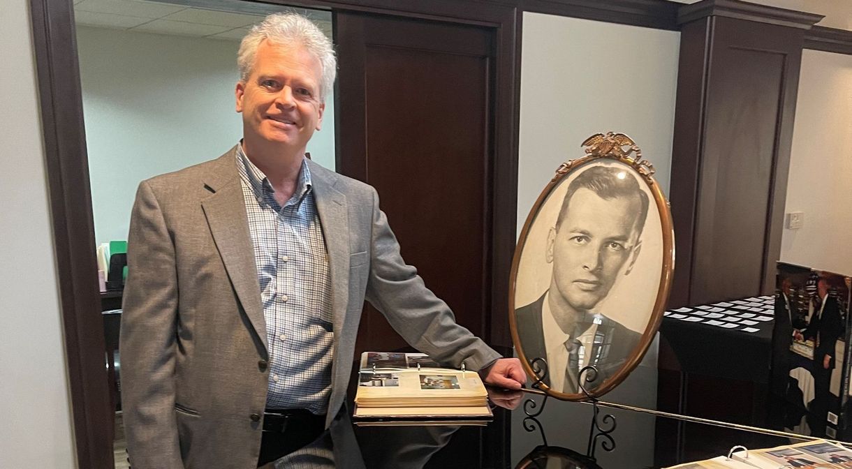 Matt Chemidlin from Family  Investors standing beside a framed portrait in an office, holding a plaque or award.