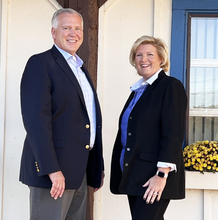 Pete Chemidlin and Darraugh Valli from Family Investors in navy blazers standing outside a building by a window box of yellow flowers