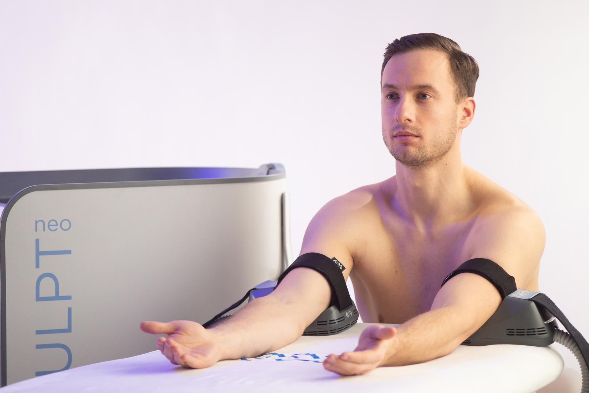 A shirtless man is sitting on a table with his arms outstretched.