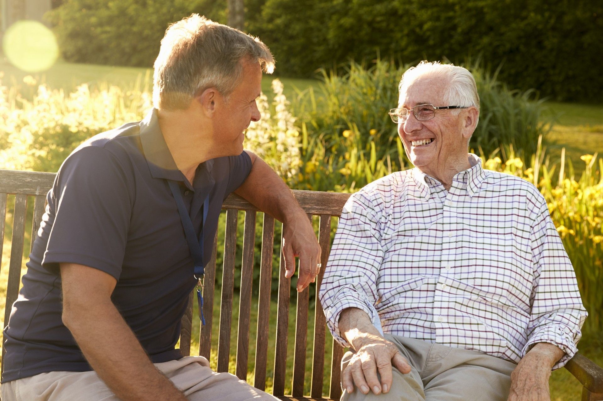 Two people sit on a park bench smiling in warm sunlight.