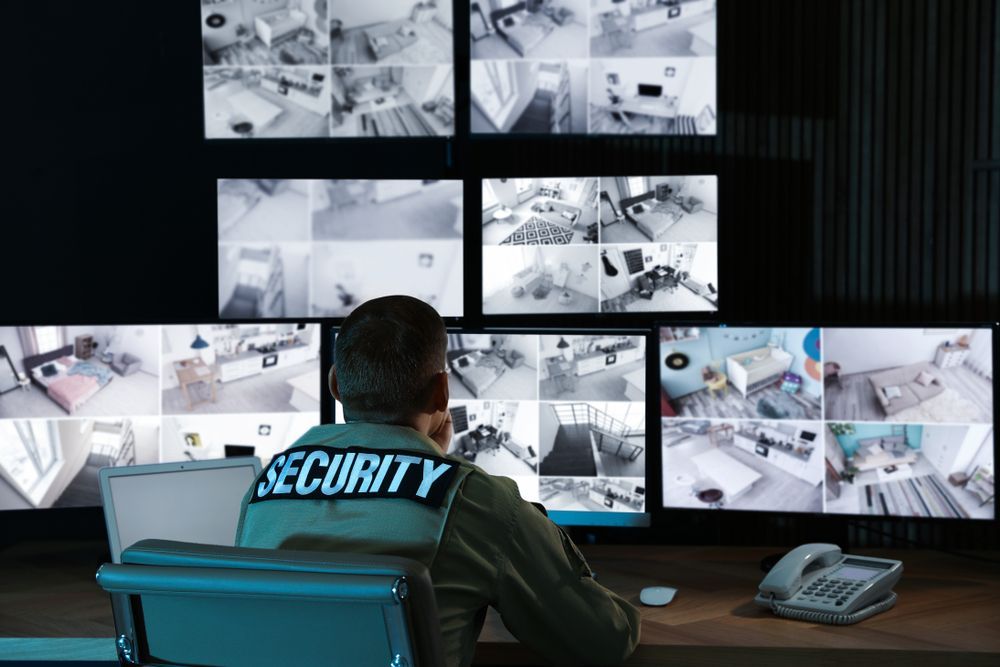 A Security Guard Is Sitting At A Desk In Front Of A Wall Of Monitors — Asset Security Group In King Creek, NSW