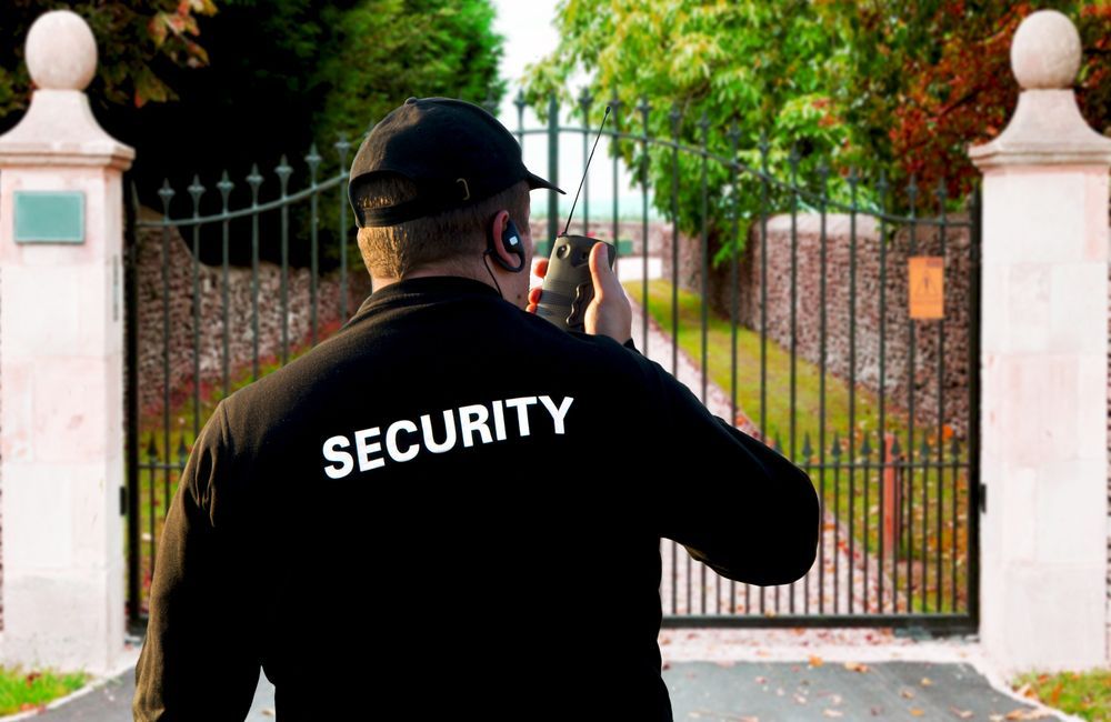 A Security Guard Is Standing In Front Of A Gate Talking On A Walkie Talkie — Asset Security Group In King Creek, NSW