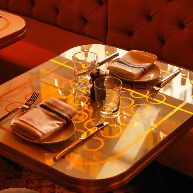 Square table set for two with plates, glasses, silverware, and napkins; orange and gold accents.