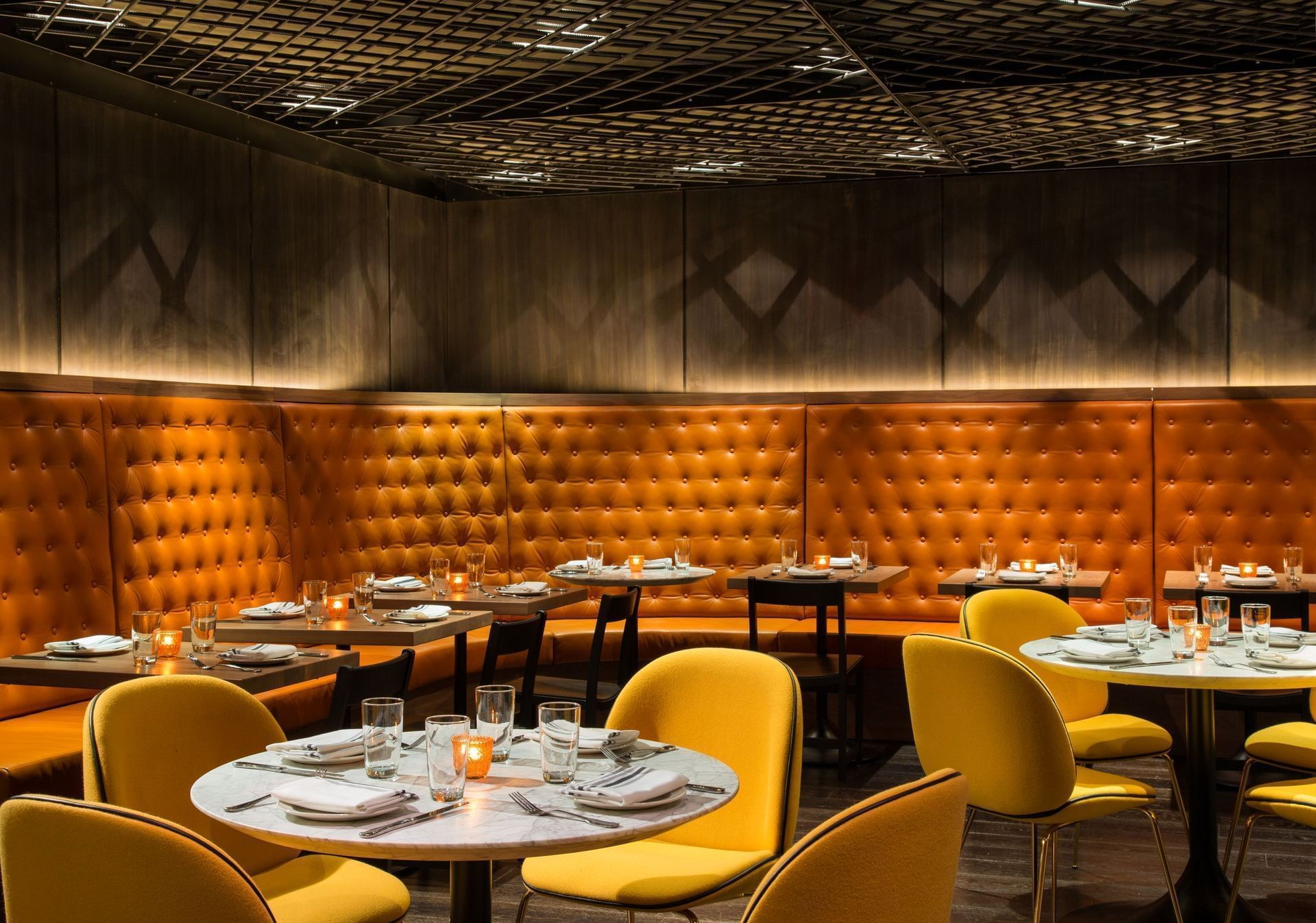 Restaurant interior with mustard-colored booths, chairs, and tables.  Dark wood paneling and decorative ceiling.
