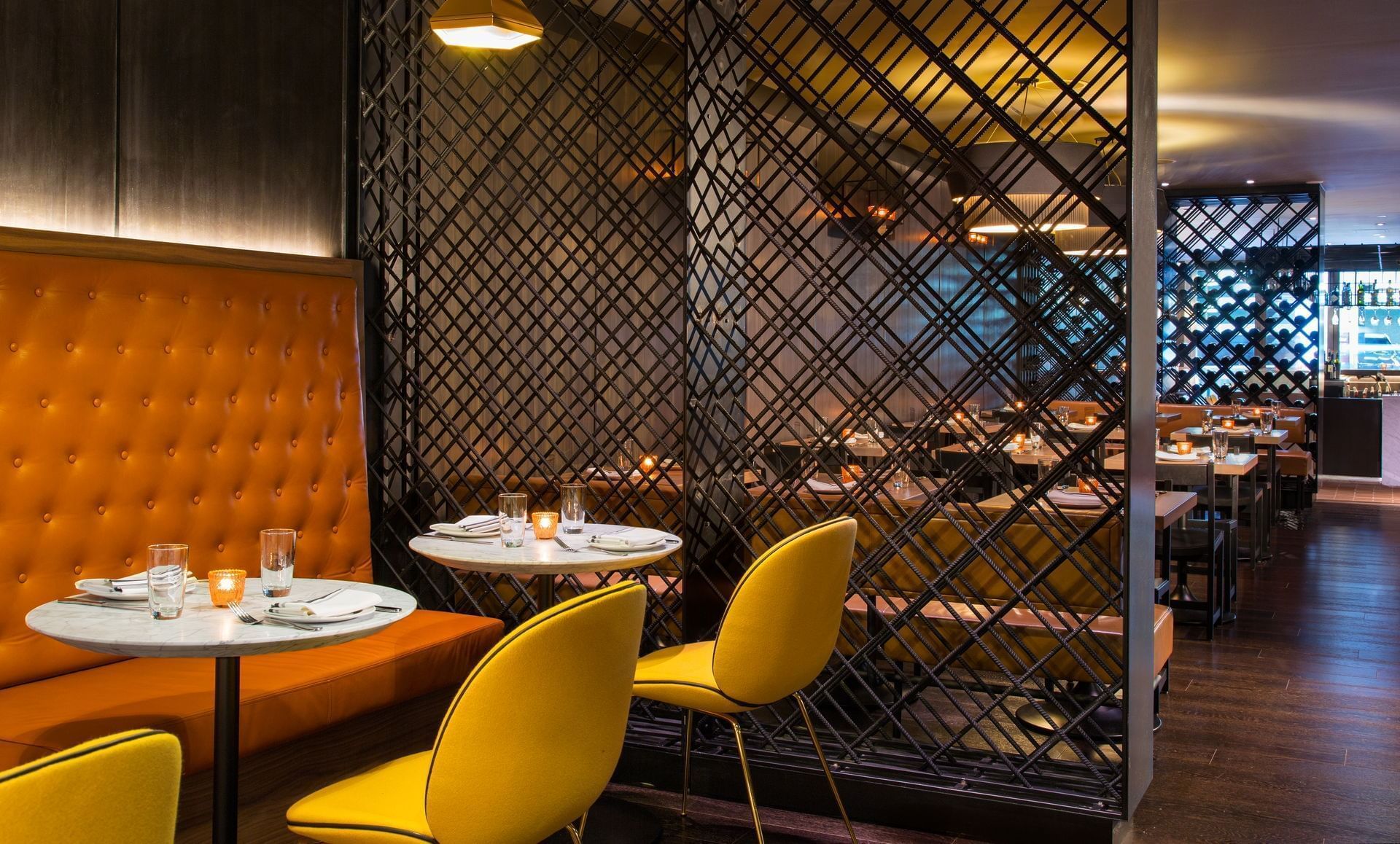 Restaurant interior: orange booth, yellow chairs, decorative metal screen, tables set with place settings.