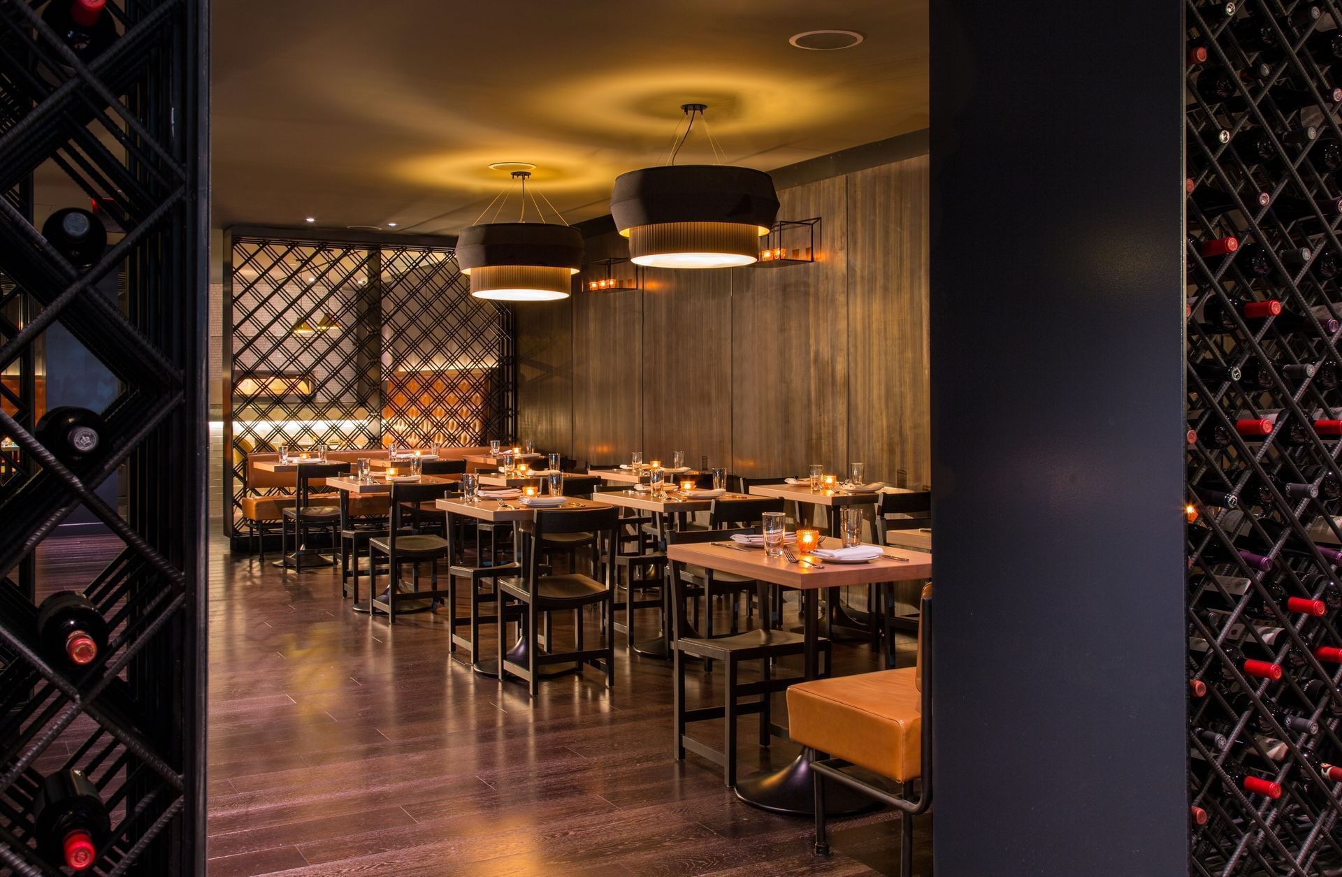 Restaurant interior with tables, chairs, and wine racks; dimly lit with overhead lamps.