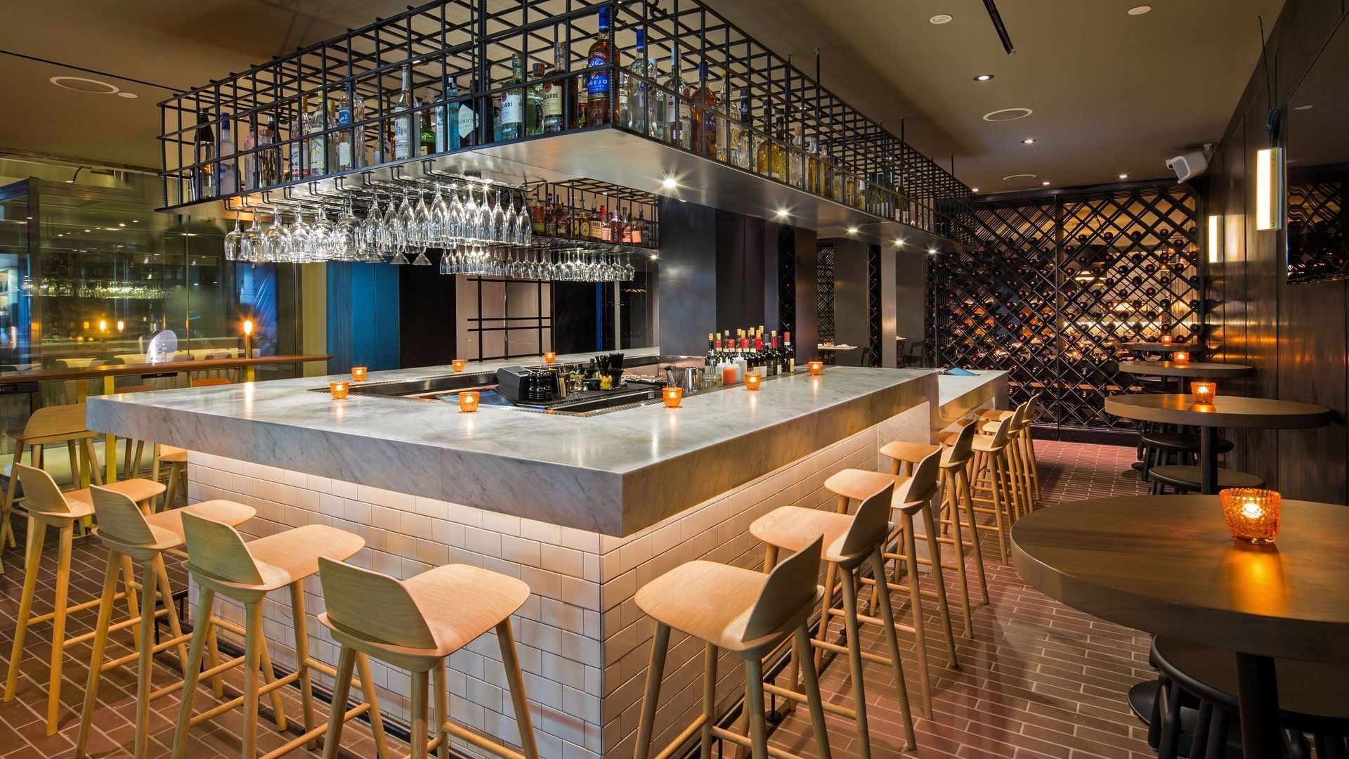 Modern bar with illuminated counter and stools, drinks hanging above.