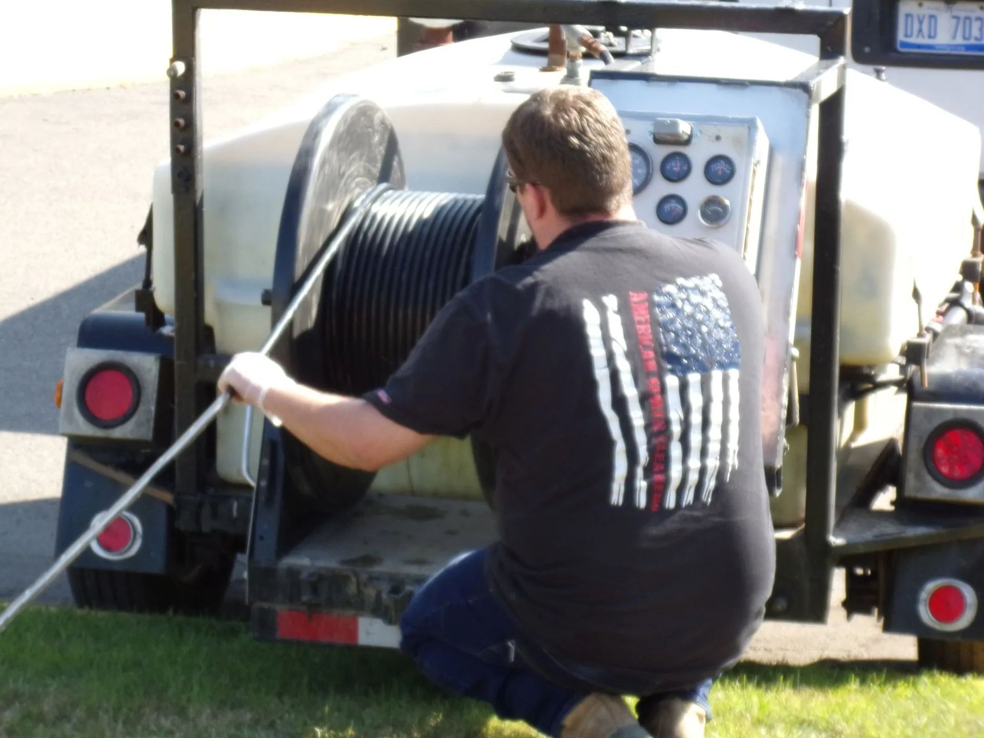Man in black shirt with American flag logo, using a cable reel on a trailer.