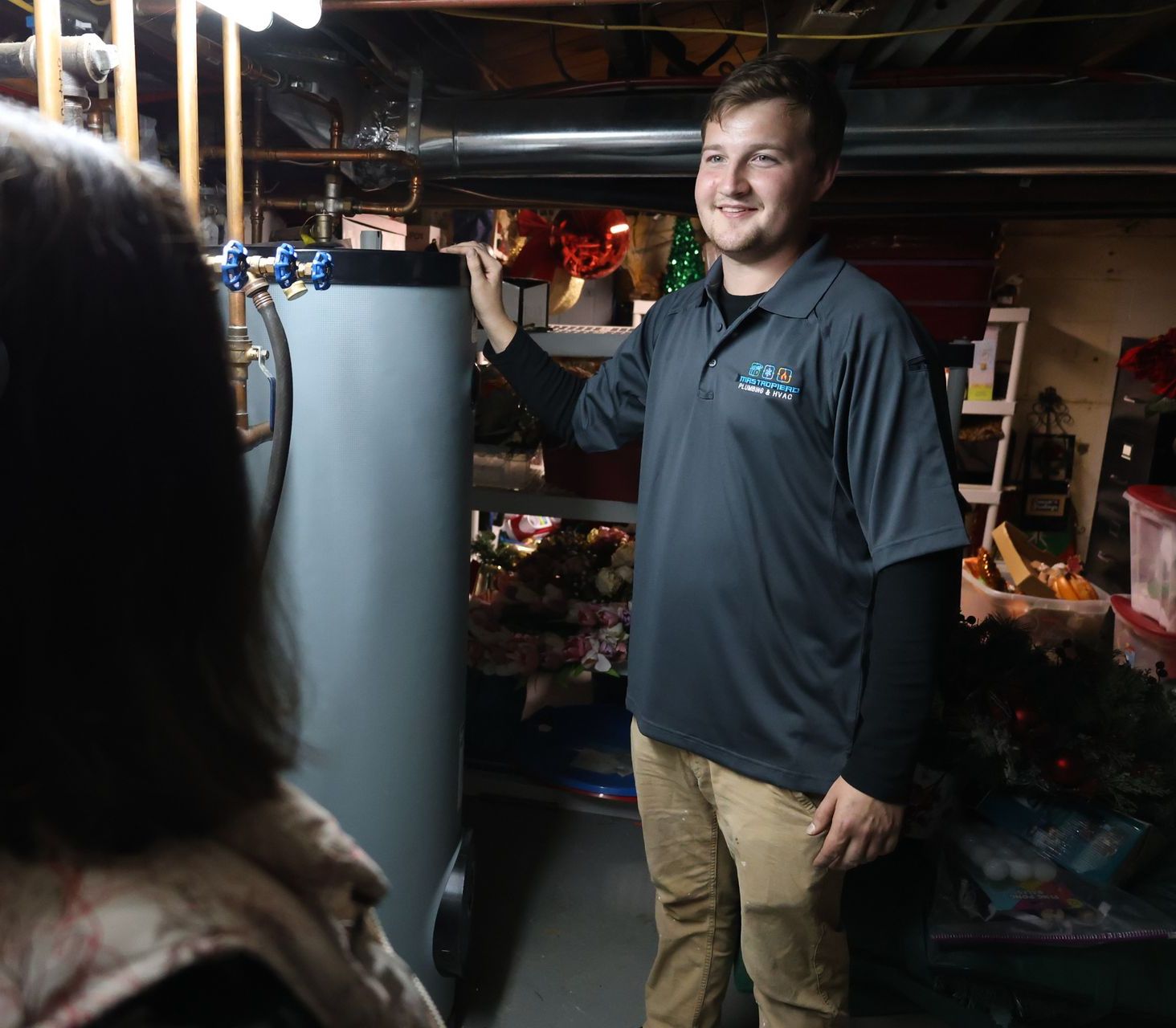 Plumber in a black shirt is standing in front of a water heater