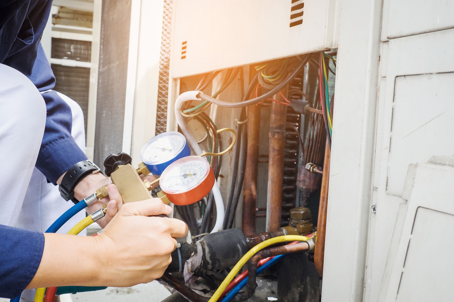 Technician servicing an outdoor air conditioning unit with gauges and hoses.
