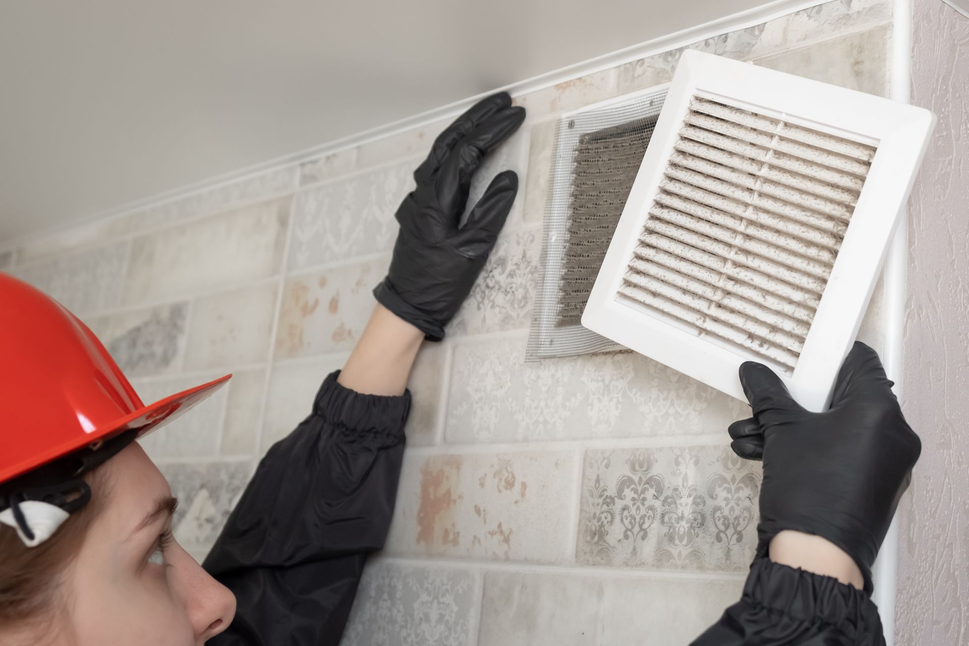 Person in black gloves and red hard hat replacing a dirty vent cover.