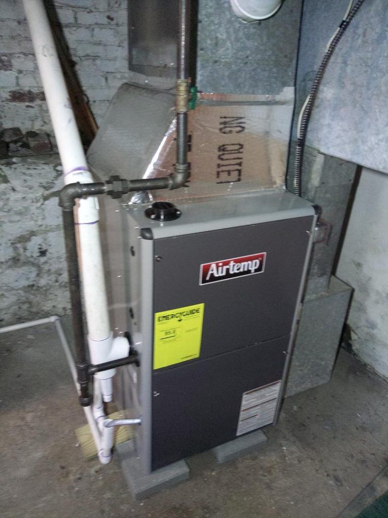 An Airtemp furnace in a basement setting, with pipes and ductwork visible.