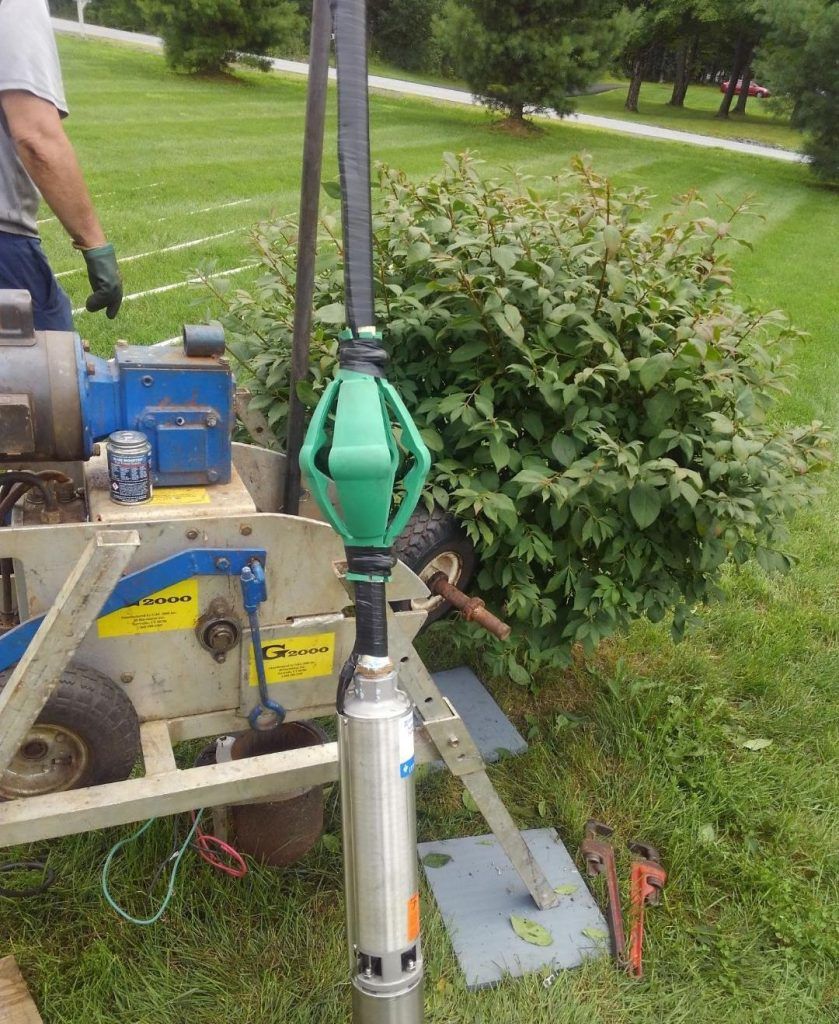 Well pump being installed outdoors near green bushes and grass. A person is present.