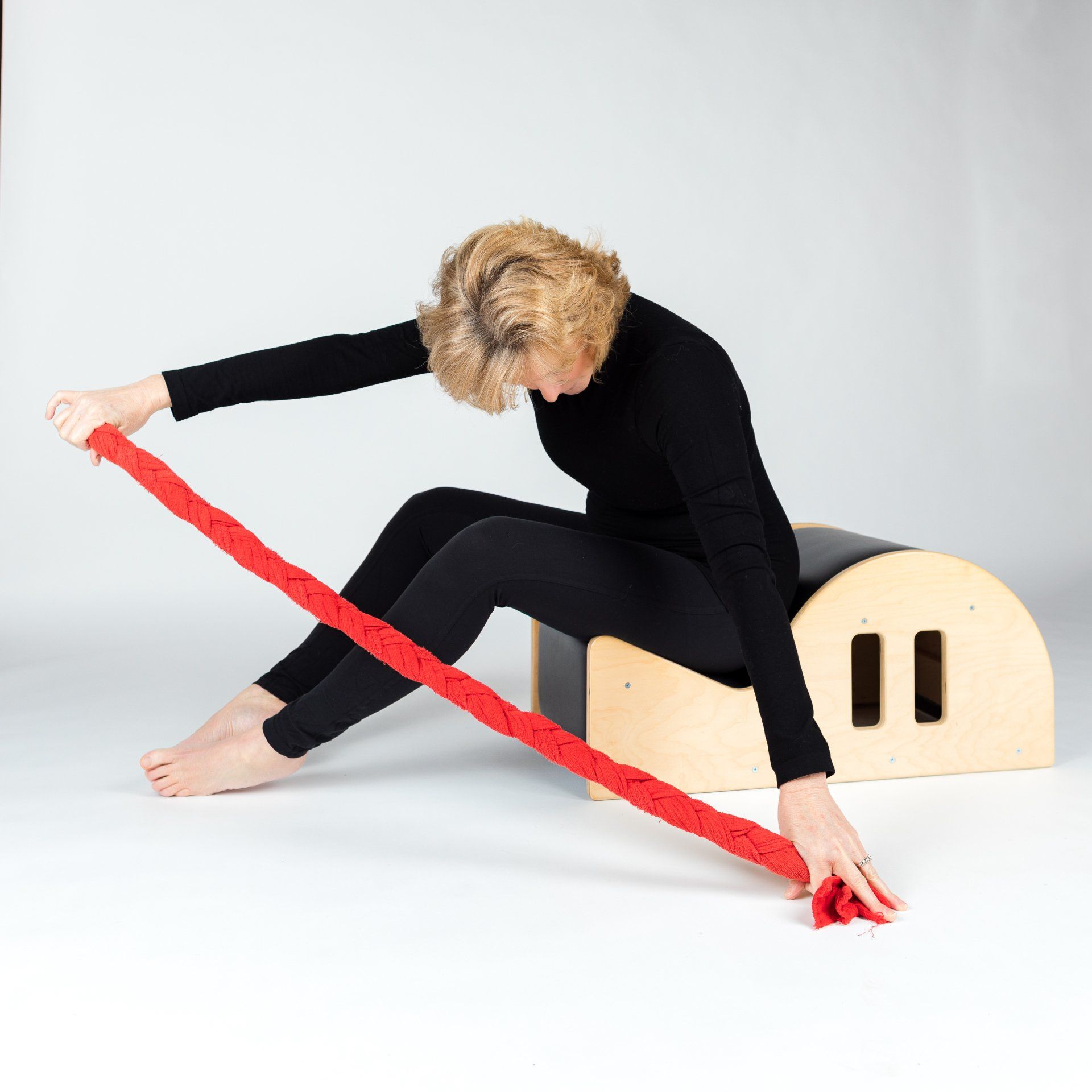 A woman is using a red resistance band to stretch her legs