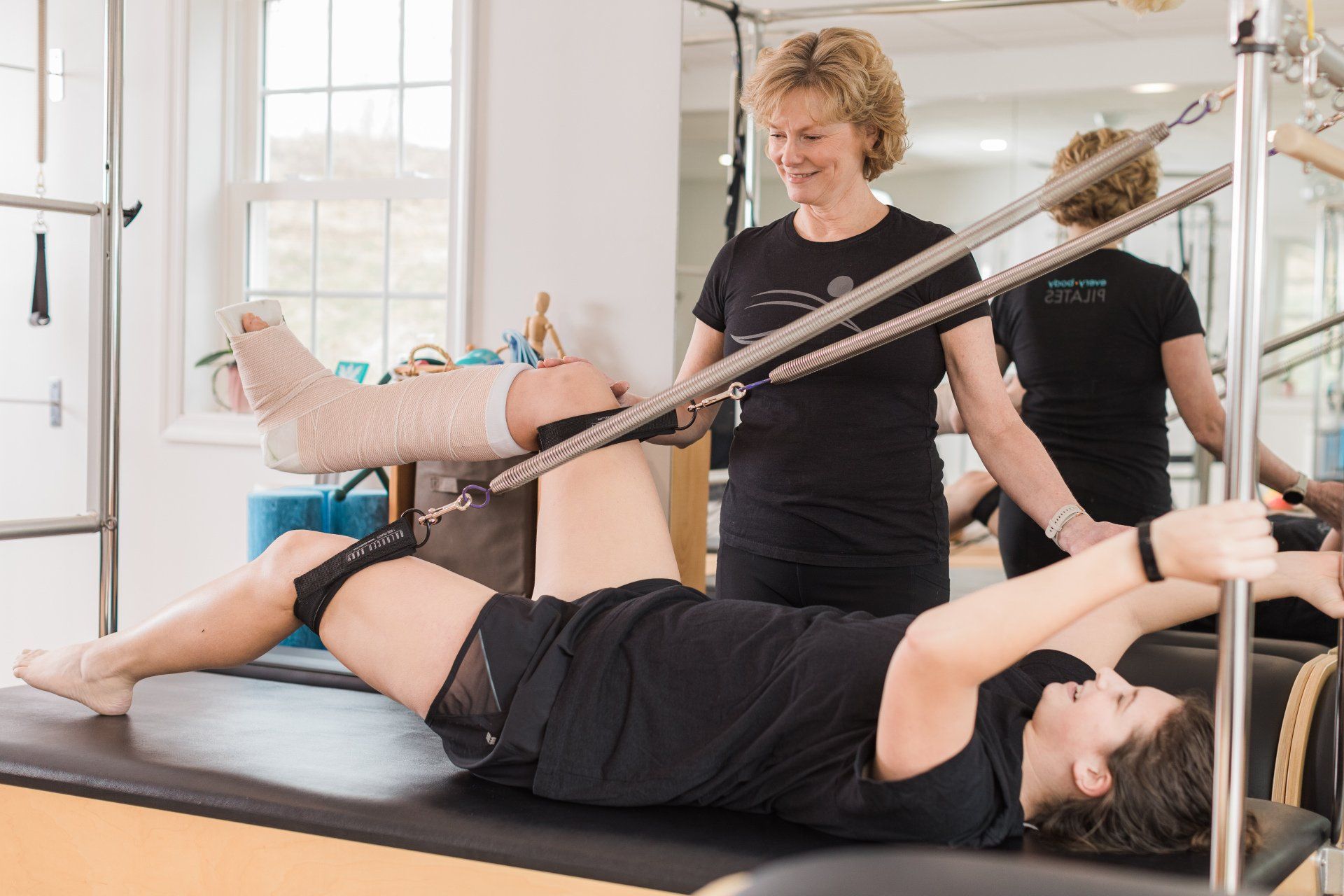 A woman with a cast on her leg is laying on a pilates machine.