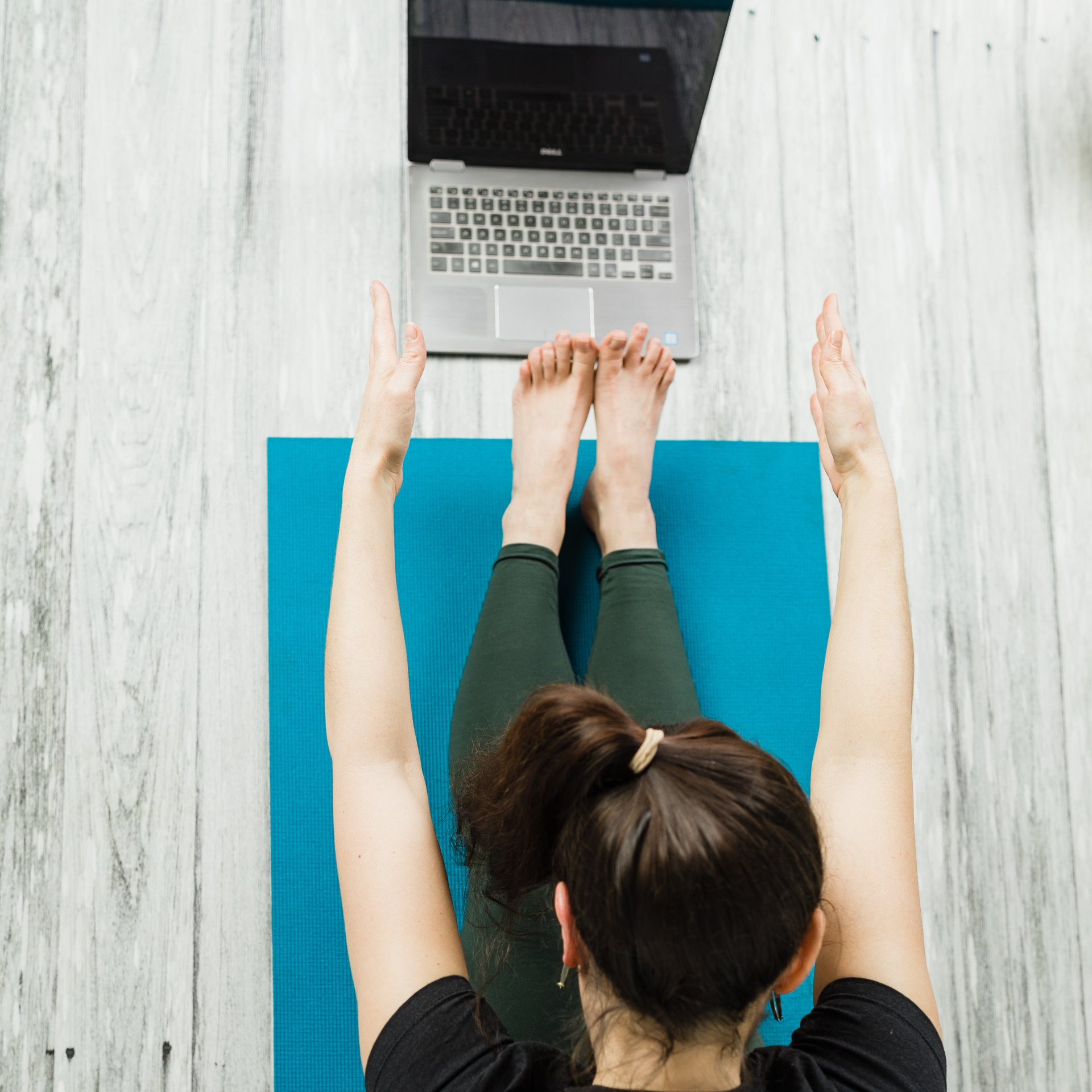 A woman is laying on a yoga mat in front of a laptop computer.