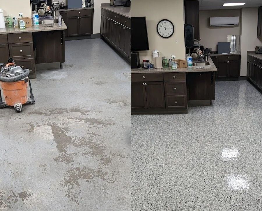 Industrial room with gray speckled floor, workbench, cabinets, wall clock, and an orange vacuum in the foreground