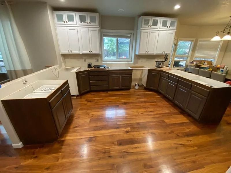 Modern kitchen with white upper cabinets, dark lower cabinets, wood floors, and a central window