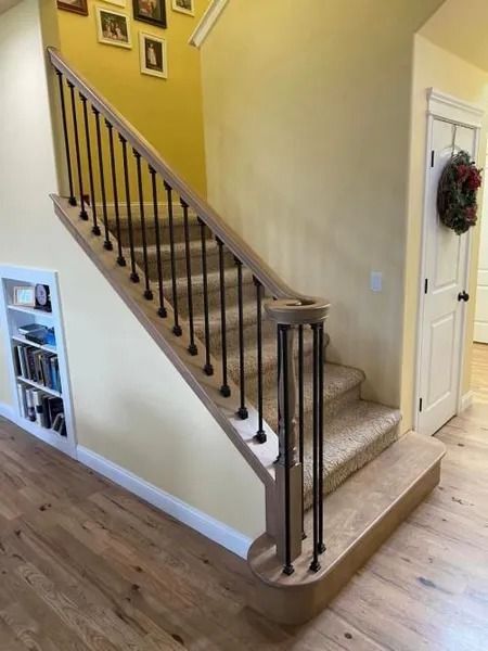 Staircase with carpeted steps, dark wood railing, and yellow walls in a home hallway