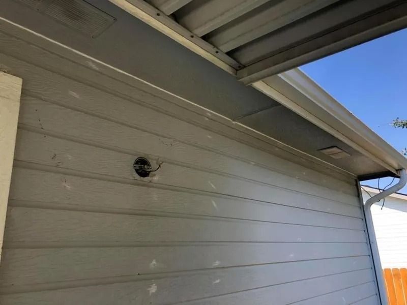 Gray house exterior under eaves with a small round vent and blue sky overhead
