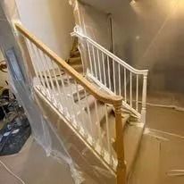 Staircase under renovation, wrapped in plastic sheeting with white railings and a wooden handrail.
