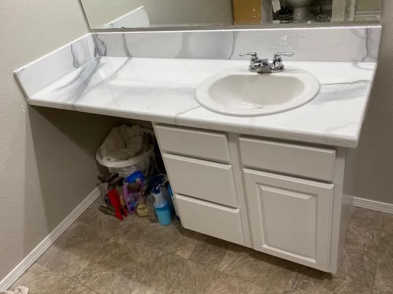 Bathroom vanity with white countertop, sink, mirror, and storage cabinets; cleaning supplies tucked underneath.
