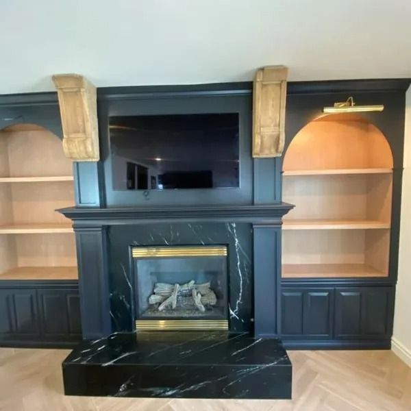 Black fireplace with mounted TV, built-in shelves, and dark cabinetry in a living room.