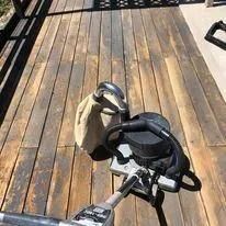 Black bicycle or scooter with tan bag on a sunlit wooden deck