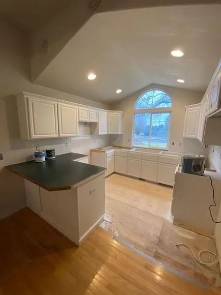Bright kitchen with white cabinets, dark countertops, wood floors, and a large arched window.