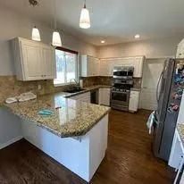 Modern kitchen with granite island, white cabinets, stainless appliances, and dark wood floors.